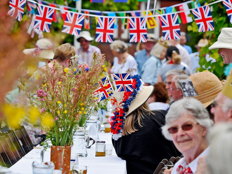 People on a long table at a street party with Union Jack bunting